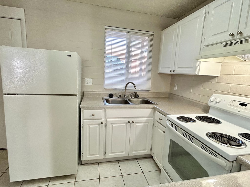 A white kitchen with a refrigerator, stove, and sink.
