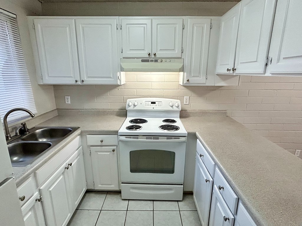 A white kitchen with a stove, sink, and cabinets.