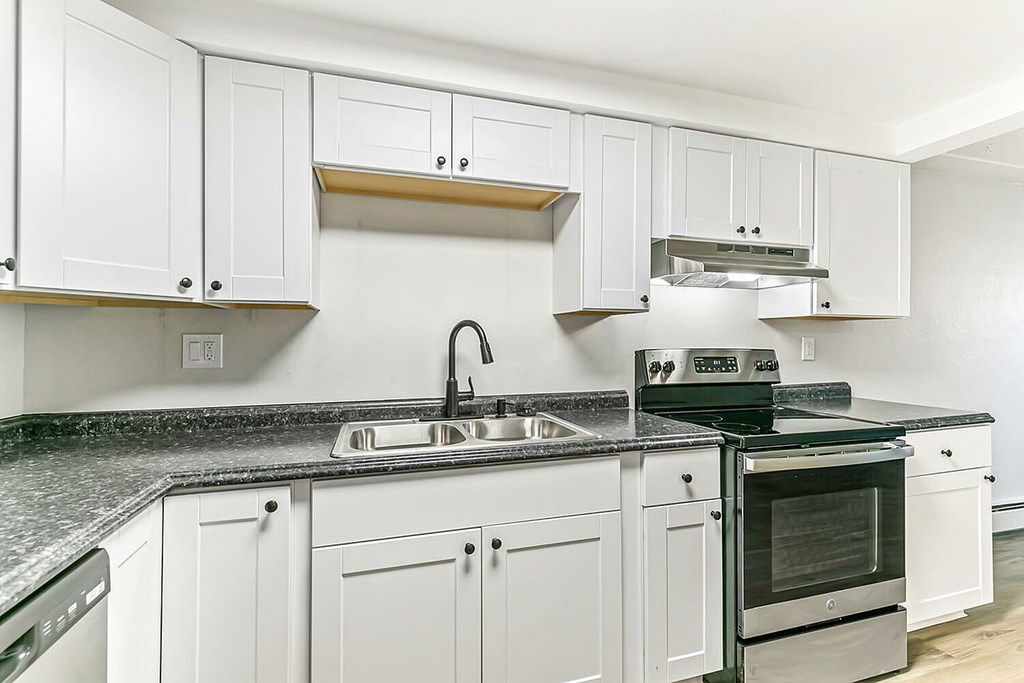 A kitchen with white cabinets and a black countertop.