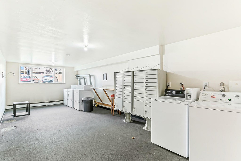 A white washing machine is in a room with a white wall and a white floor.