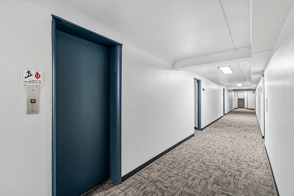 A long hallway with a blue door and a sign on the wall.