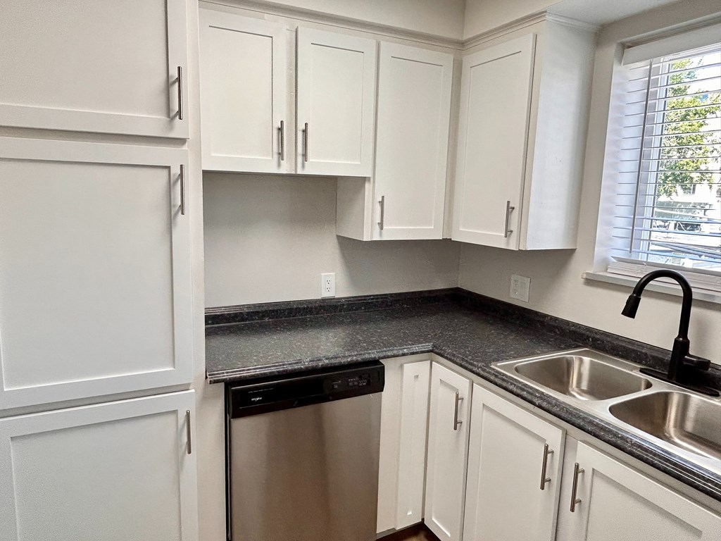 A kitchen with white cabinets and a black countertop.