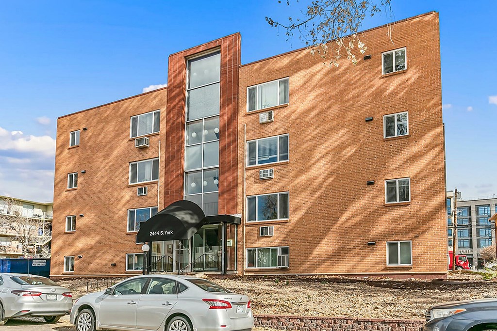 A red brick building with a black awning and a silver car parked in front.