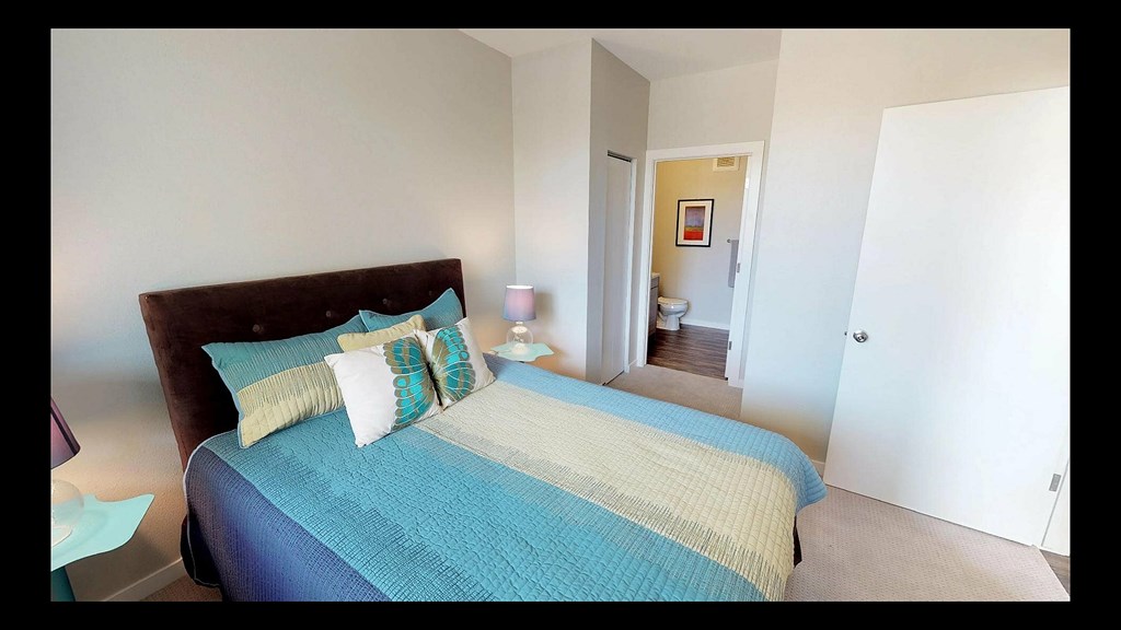 A bed with a blue and yellow comforter is in the foreground of a room.