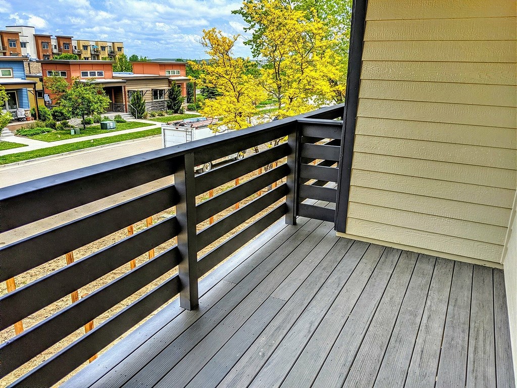 A wooden deck with a railing overlooking a residential area.