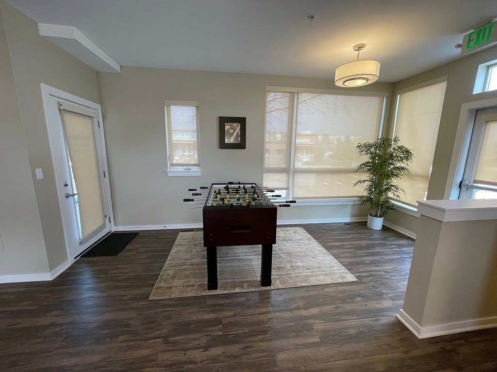 A room with a chess table in the middle and a plant on the right side.