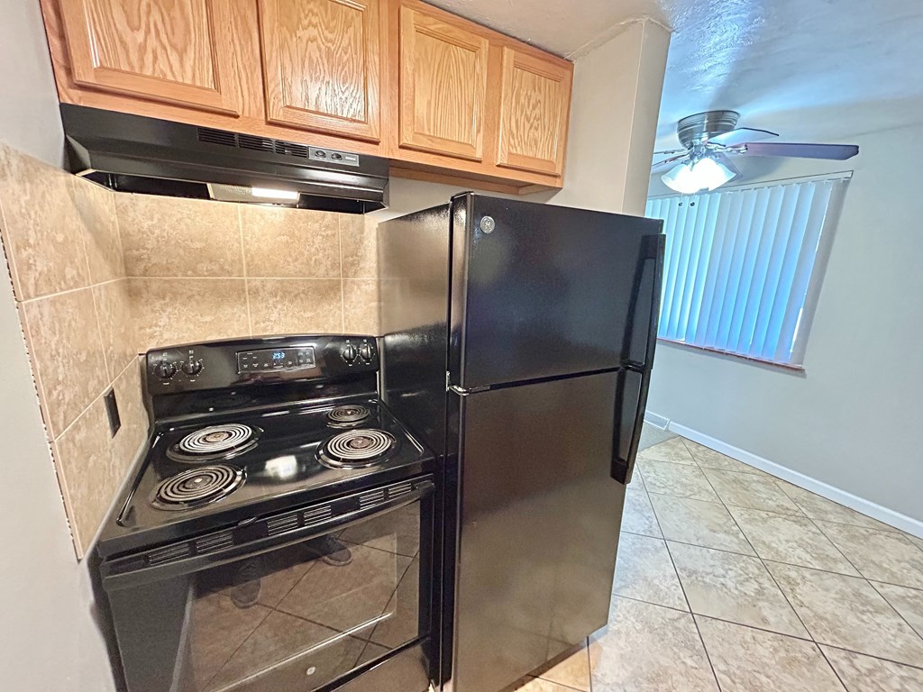 A black refrigerator is in a kitchen with a stove and wooden cabinets.
