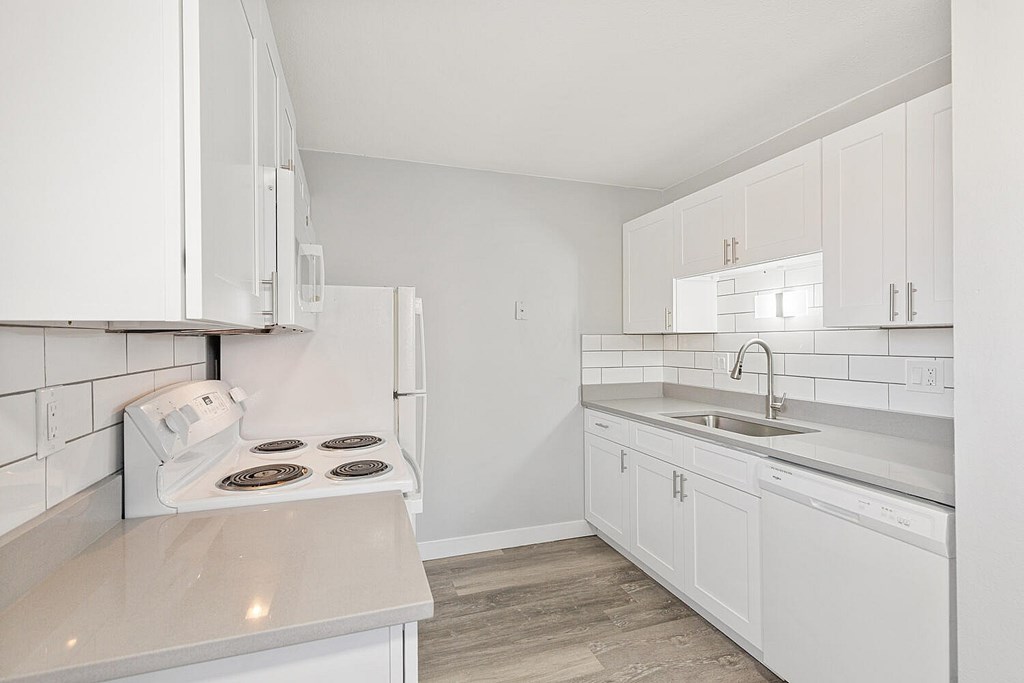 A white kitchen with a stove, sink, and cabinets.