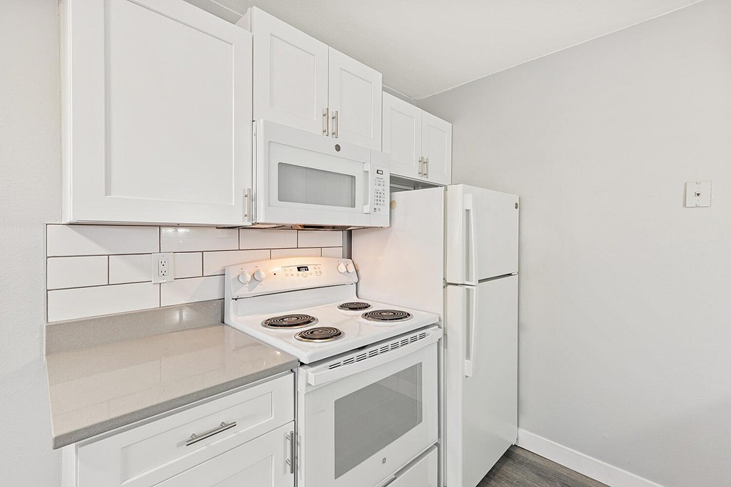 A white kitchen with a stove, microwave, and refrigerator.