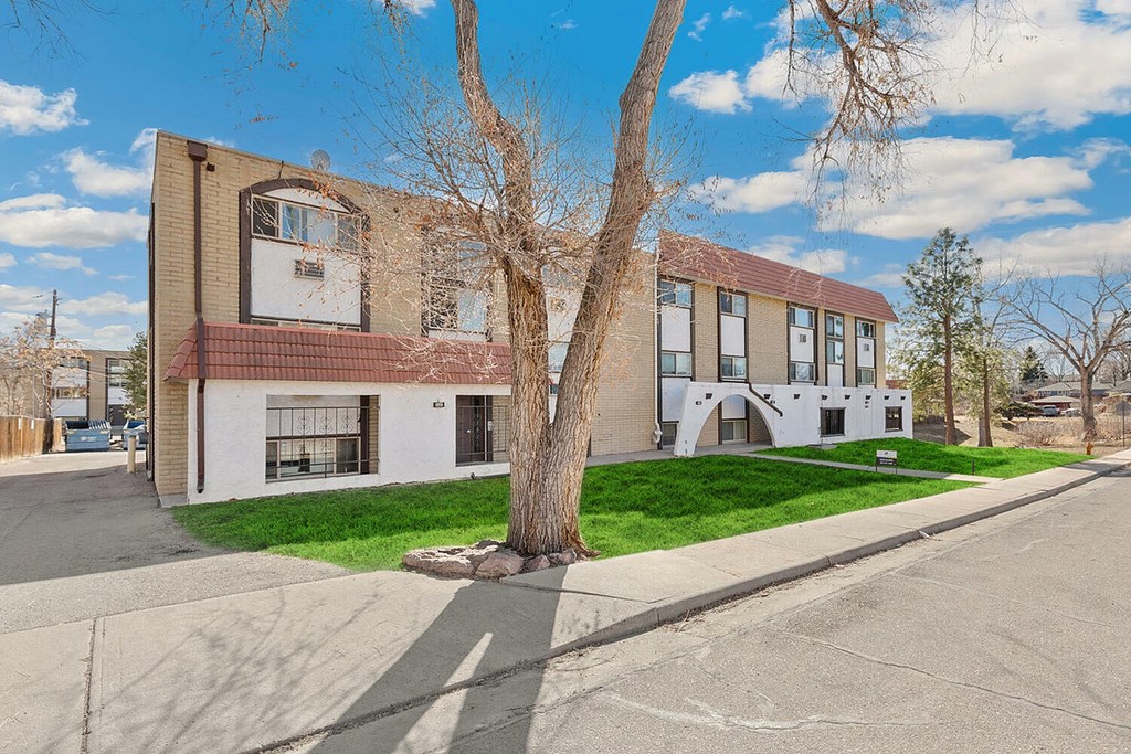 A tree stands in front of a two-story building with a white and brown facade.