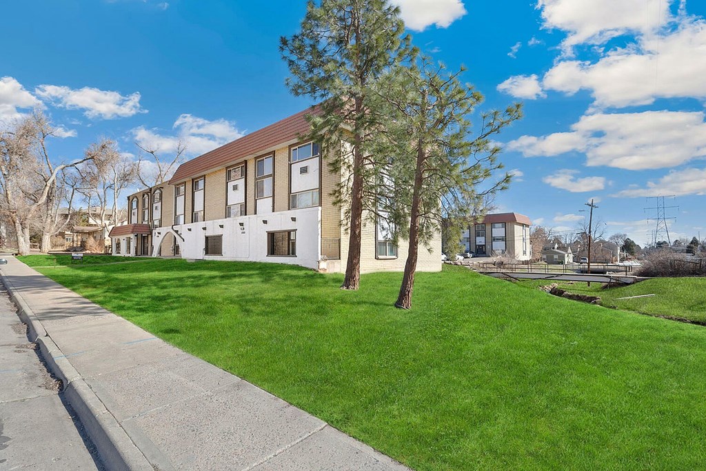A building with a brown roof and white walls is surrounded by a grassy area and a sidewalk.
