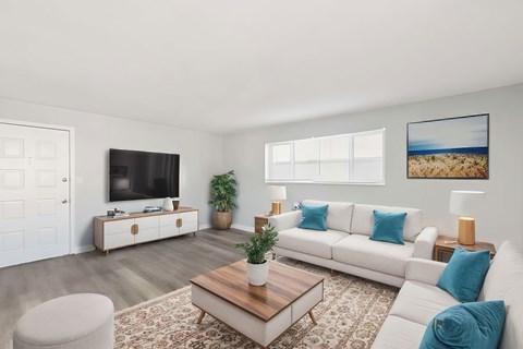 A living room with a white couch, a wooden coffee table, and a flat-screen TV on a cabinet.