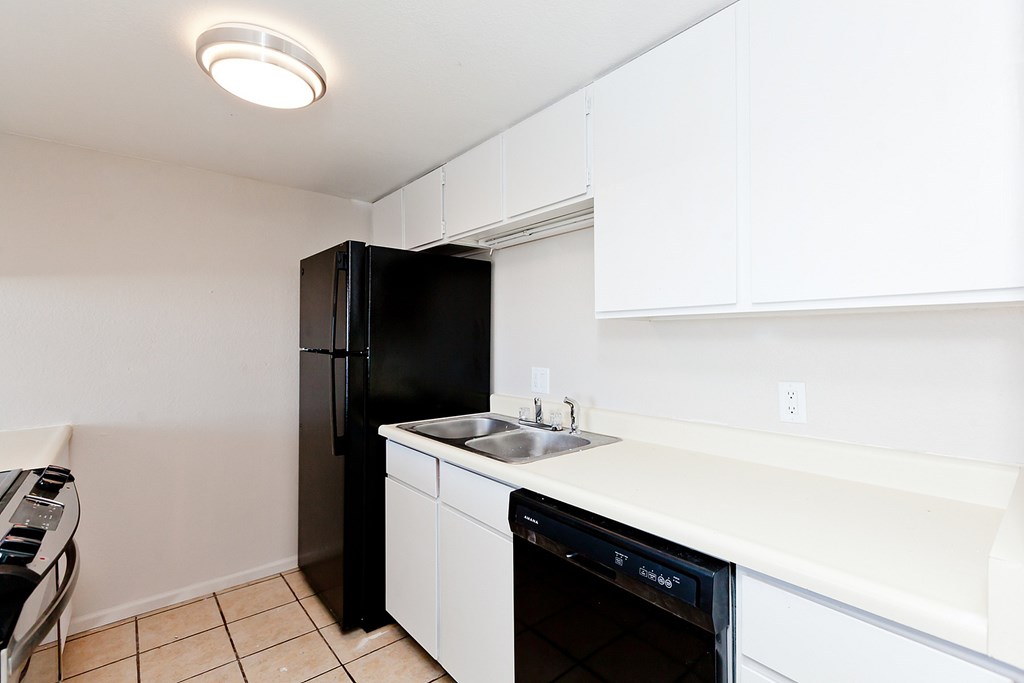 A black refrigerator is in a kitchen with white cabinets.