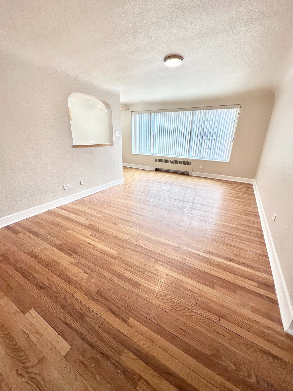 A room with wooden flooring and a window with blinds.