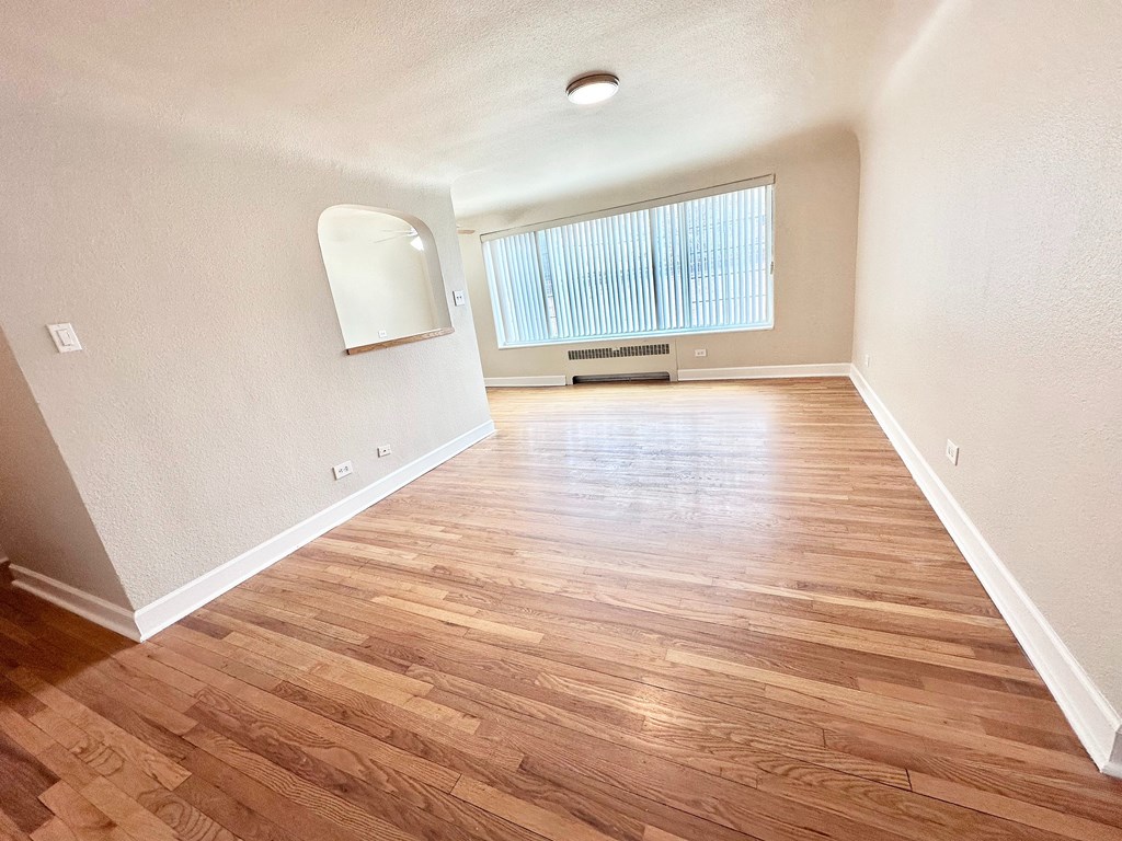 A room with wooden flooring and a window with blinds.