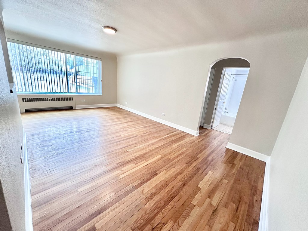 A room with wooden flooring and a window with blinds.