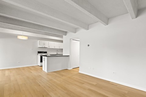 A kitchen with white cabinets and a white fridge is in a room with wooden floors and white walls.