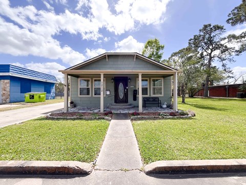 A small house with a grey roof and a blue door is surrounded by a grassy lawn.