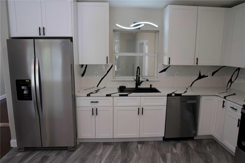 A kitchen with a stainless steel refrigerator and white cabinets.