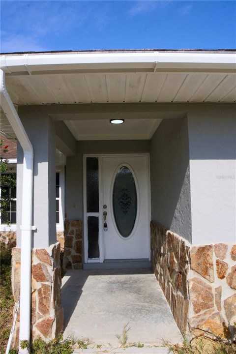 A white door with a glass window is set in a white wall with a stone pillar on each side.