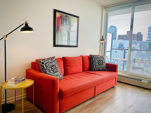A red couch with two pillows sits in a room with a lamp and a picture on the wall.