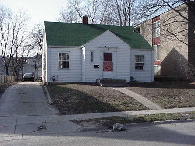 A white house with a green roof sits on a street corner.