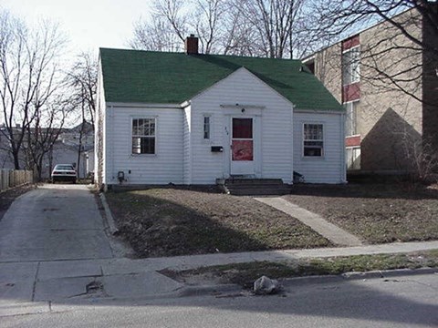 A white house with a green roof sits on a street corner.