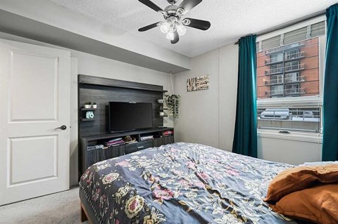 A bedroom with a bed, a television, and a ceiling fan.