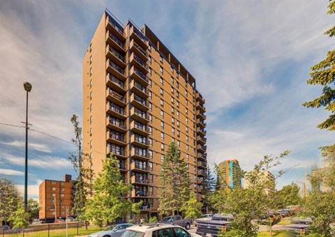 A tall apartment building with a parking lot in front.