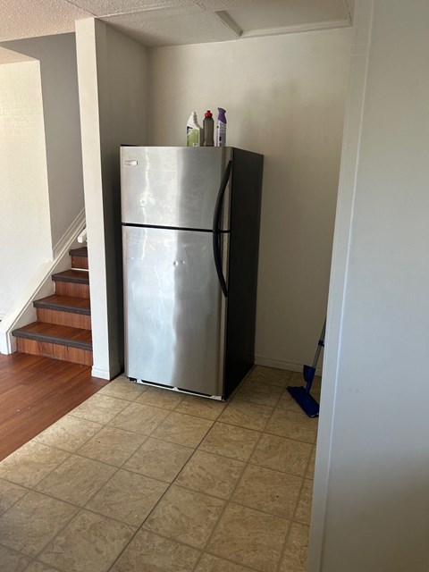 A silver refrigerator in a kitchen with a blue mop on the floor.