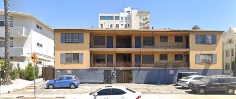 A yellow and white building with a blue car parked in front.