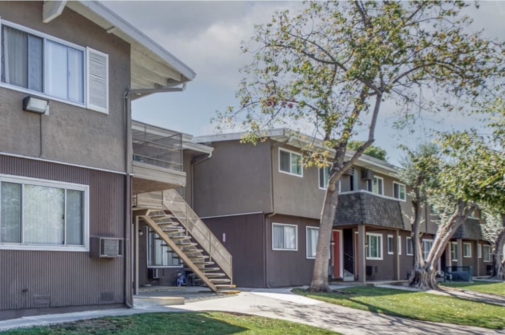 A tree in front of a brown house with a red door.