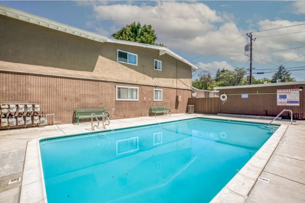A small pool in a backyard with a brown building behind it.