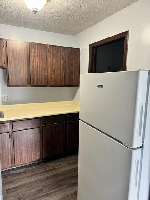 A white refrigerator stands in a kitchen with wooden cabinets.