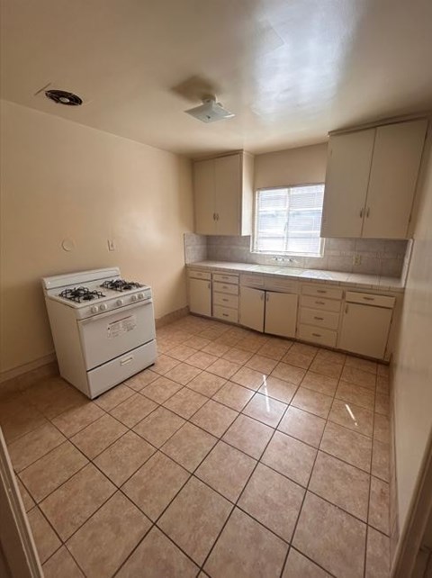 A kitchen with a stove, cabinets, and a window.