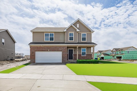 A house with a grey garage door is in front of a green field.