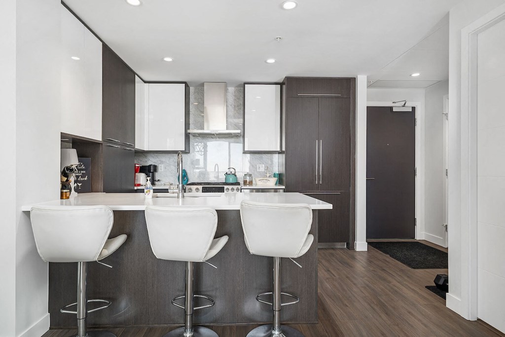 A modern kitchen with white bar stools and a dark wood floor.