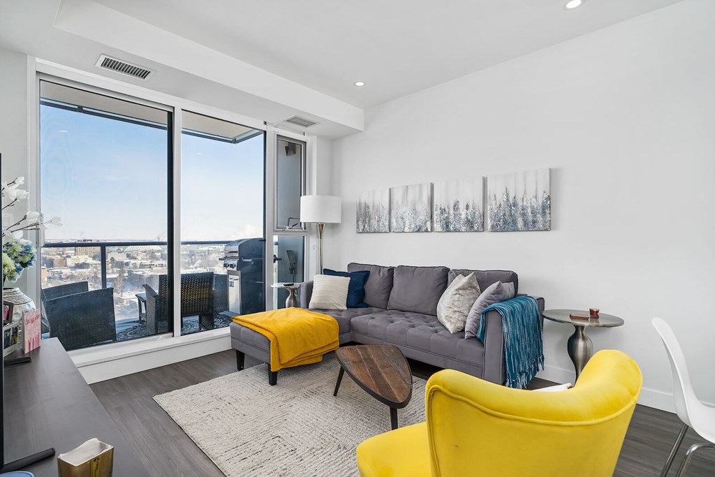 A living room with a grey couch, yellow chair and a painting on the wall.