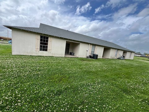 A large building with a grey roof and a grassy field in front of it.