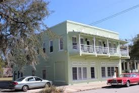 A green two-story building with a balcony and a car parked in front.