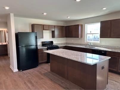 A kitchen with a black refrigerator and brown cabinets.