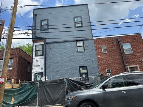 A grey car is parked in front of a grey and black building.
