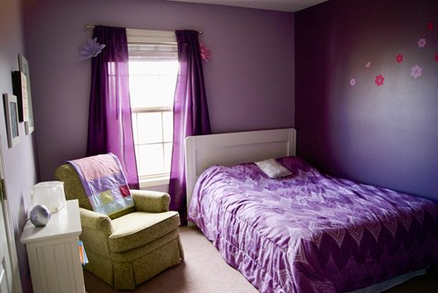 A bedroom with a purple bed and a chair.