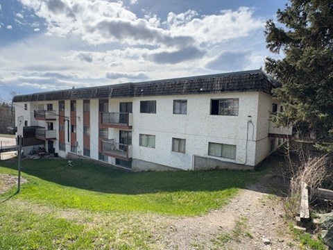 A white building with a black roof and a green lawn in front.