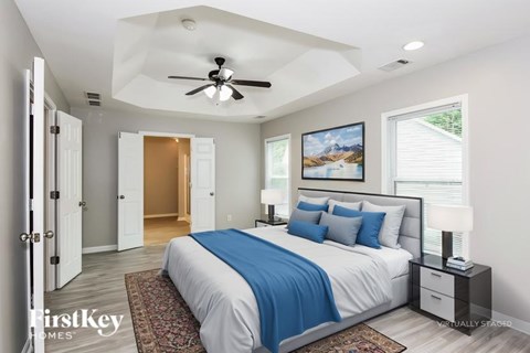 A bedroom with a bed, a ceiling fan, and a painting on the wall.