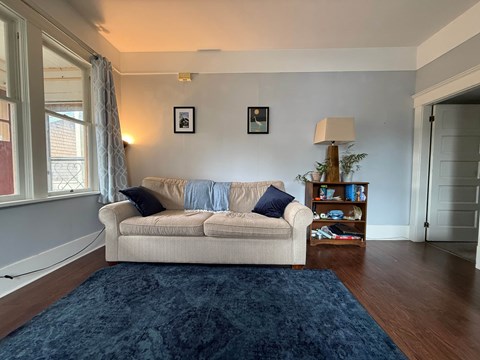 A living room with a beige couch, a blue rug, and two picture frames on the wall.