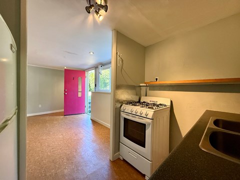 A kitchen with a white stove and a pink door in the background.