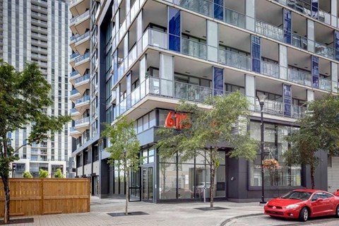 A red car is parked in front of a modern building with a glass facade.