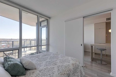 A bedroom with a large bed and a balcony with a view of the city.