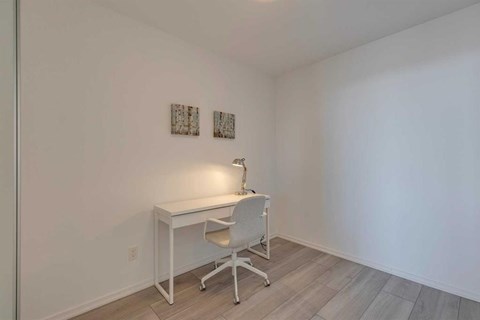 A white desk with a chair and a lamp on a white wall.